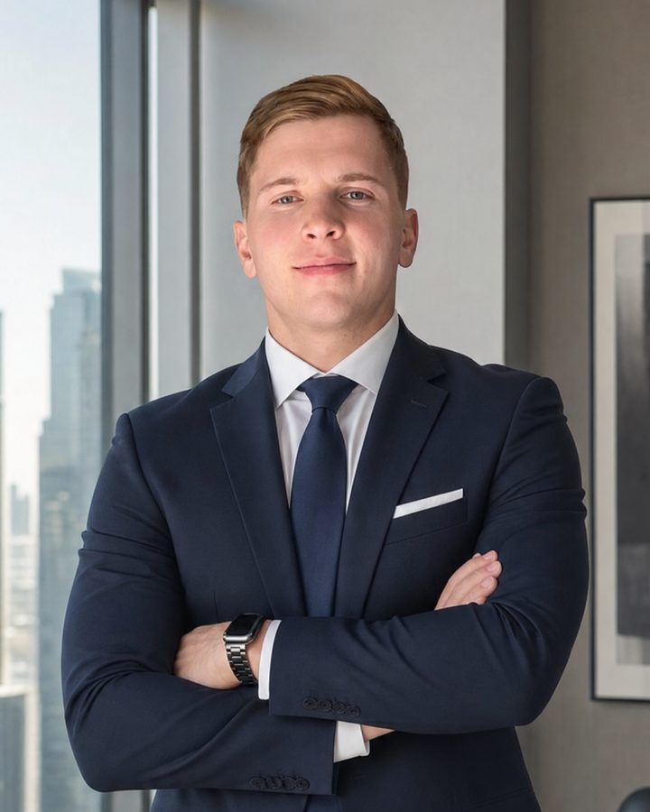 Emil Fabel in a navy suit and tie, arms crossed, in an office